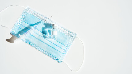 Vaccination concept. COVIC-19 coronavirus vaccine. White table with blue surgical mask, vaccine...