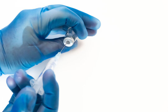 Vaccination concept. COVIC-19 coronavirus vaccine. Doctor's hands with blue gloves holding the vaccine vial bottle and syringe. White background.