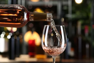 Fotobehang Pouring rose wine from bottle into glass on blurred background, closeup © New Africa