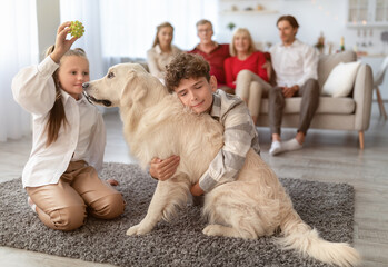 Adorable kids playing and hugging pet dog while their big family relaxing on sofa in living room