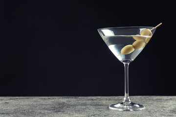 Martini cocktail with olives on grey table against dark background, space for text