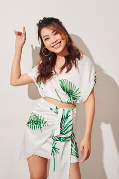 A young and attractive Asian girl in a dress smiling and posing against a white background