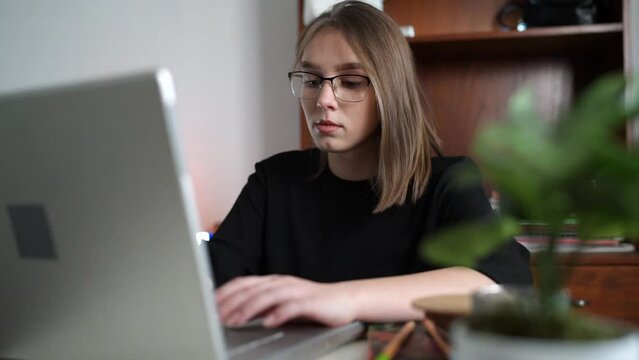 One young caucasian woman female student working on her laptop computer sitting at the table at home writing typing online learning and education concept checking test results or online chat 