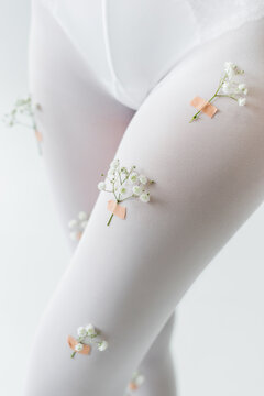cropped view of woman in tights decorated with gypsophila flowers isolated on light grey.