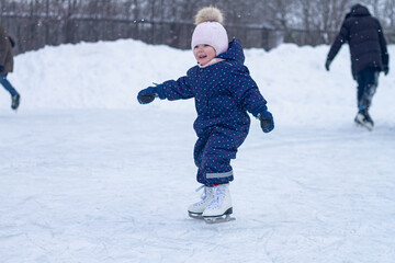 Baby girl 2 years old rides white figure skates in winter at the ice rink