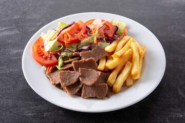 Plate of kebab, vegetables and french fries on black background