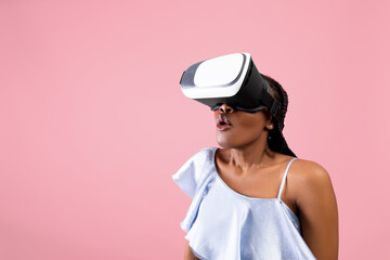 Surprised black lady in VR glasses exploring cyberspace, playing online game in virtual reality on pink background