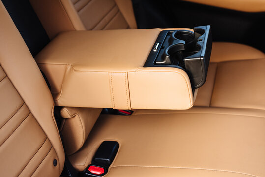 Leather folding armrest armrest with cup holders in rear seats inside a vehicle. Clean leather interior: yellow rear seats, headrests and belts.