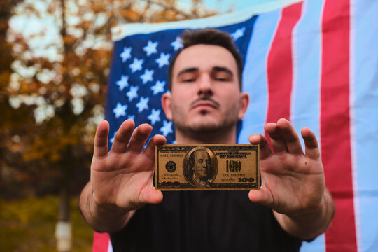Successful young man holding golden dollar bills with a USA flag on the background