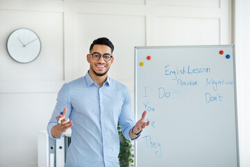 Arab male teacher giving remote class, standing near blackboard, explaining English rules to pupils...