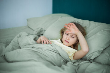 A little girl lies in bed and is sick, feeling unwell and having a cold in the winter