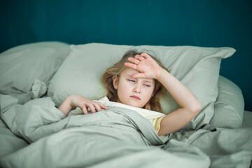 A little girl lies in bed and is sick, feeling unwell and having a cold in the winter