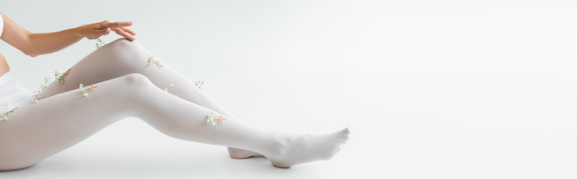 cropped view of woman with tiny flowers on tights sitting on light grey background, banner.
