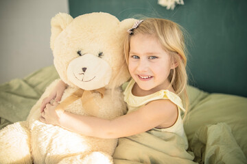 A little caucasian girl plays with a teddy bear in bed, hugs him and puts him to sleep