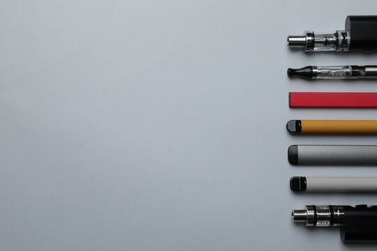 Many different electronic cigarettes on light background, flat lay. Space for text