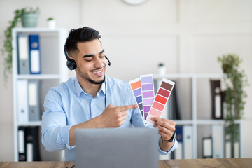 Arab guy showing color swatches at laptop in office, presenting graphic design project during remote business meeting