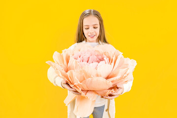 Girl holding a huge peony flower in her hands on a yellow background. Beautiful bud