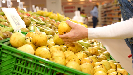 Elderly woman chooses ripe organic pears in the supermarket. Woman picks ripe organic pears in the supermarket during quarantine.