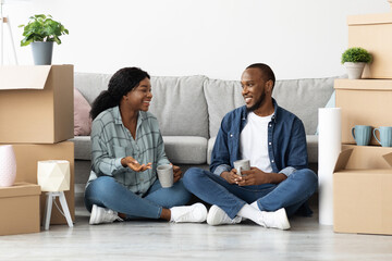 Happy Black Couple Relaxing Among Cardboard Boxes After Moving To New Flat