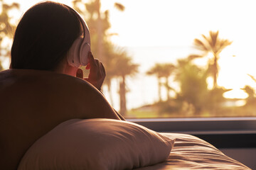 Silhouette of woman with headphones lying on pillow on the bed in bedroom opposite panoramic window...