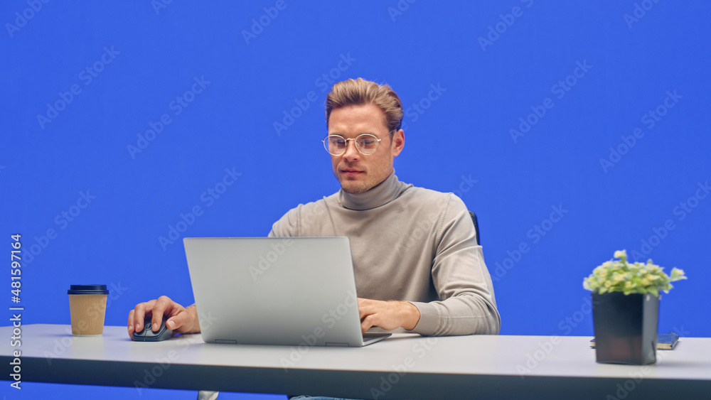 Poster modern office green screen background: young businessman sitting at his desk working on a laptop com