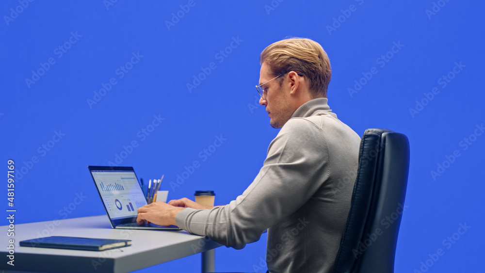 Poster modern office green screen background: businessman sitting at his desk working on a laptop computer.