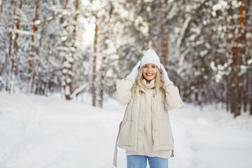 Fototapeta na wymiar Happy blonde girl in casual white clothes relaxes outdoors in winter. Snowy landscape on the background