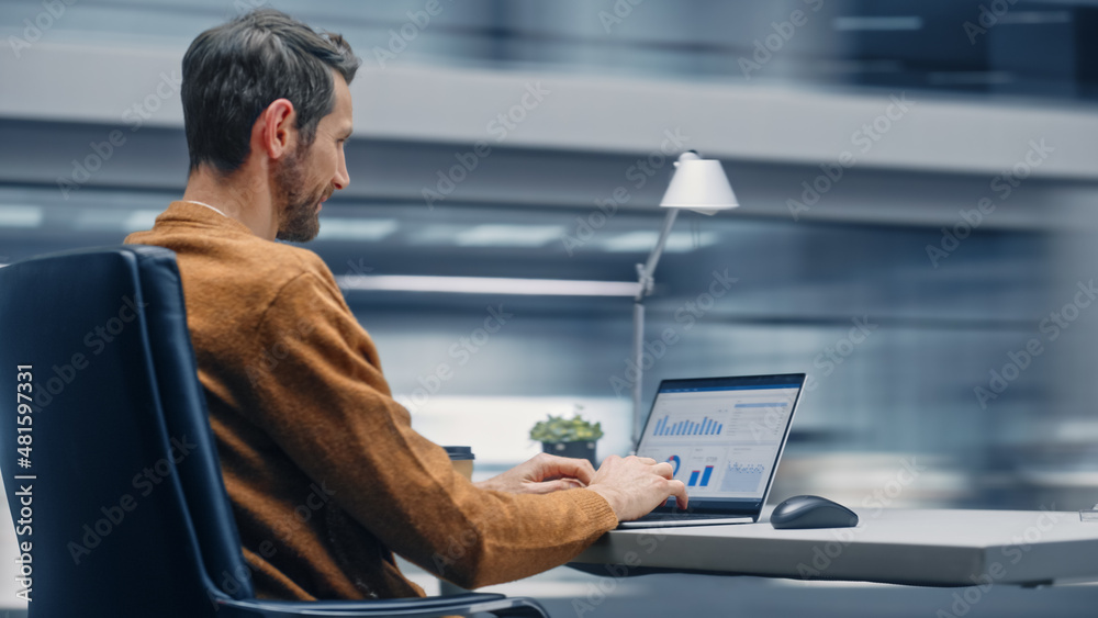Poster Modern Office: Handsome Businessman Sitting at His Desk Working on a Laptop Computer. Man working with Big Data e-Commerce Analysis. Motion Blur Background Showing Active Work Day.