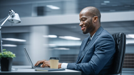 Modern Office: Successful Businessman Sitting at Desk Using Laptop Computer. African American...
