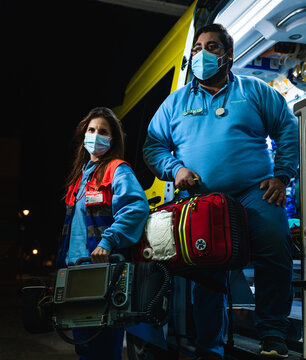 night photo of female doctor and nurse posing at the door of the ambulance with the monitor and medical backpack ready to work