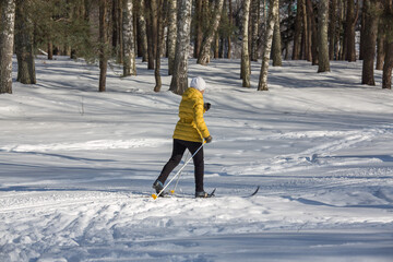 Woman skier walking by the snow in a winter park. Winter sports and leisure outdoors. Selective focus.