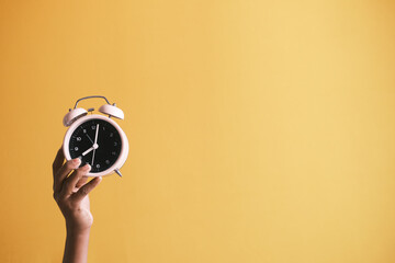  person hand holding alarm clock yellow background ,