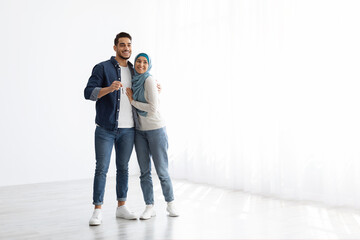 Happy muslim couple posing in empty apartment, showing key