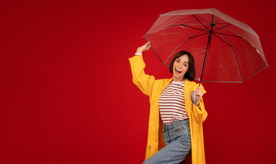 Rainy weather concept. Overjoyed young lady standing under transparent umbrella over red background, panorama © Prostock-studio