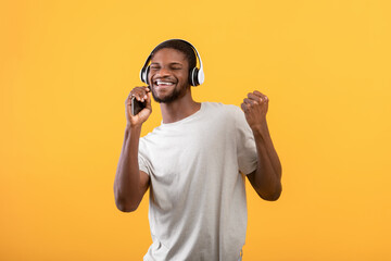 Technologies for fun. Overjoyed african american guy listening music in headphones and singing over yellow background