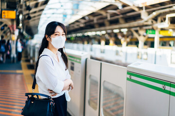マスクをして電車を待つ若い女性