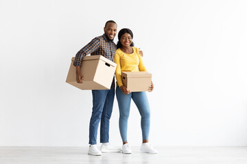Fototapeta na wymiar Happy Black Couple Standing With Cardboard Boxes In Hands In New Apartment
