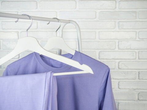 A lilac T-shirt and sweatpants hang on a hanger. Women's, youth clothes. White brick wall.