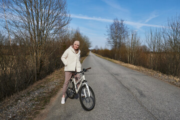 young woman cycling on the road with trees without leaves in spring