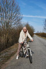 young woman cycling on the road with trees without leaves in spring