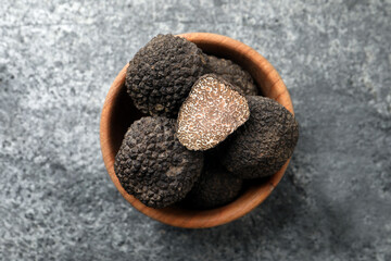 Black truffles in wooden bowl on grey table, top view