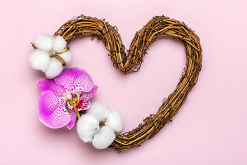 heart shaped rattan wreath decorated with tropical flowers of orchid, cotton on pink background Top view Flat lay Holiday card Happy Valentine's day, love concept Copy space