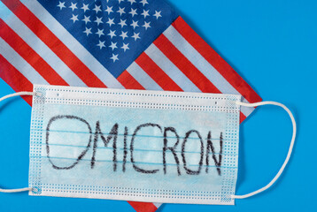 The flag of the United States of America and a medical mask with Omicron written on a blue background. Omicron is a new version of the Covid-19.