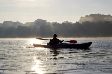 Alone woman kayaking at river at haze autumn morning