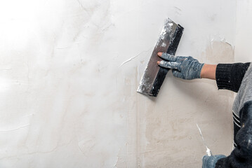 The hands of a worker level the walls with a spatula using putty during repairs.