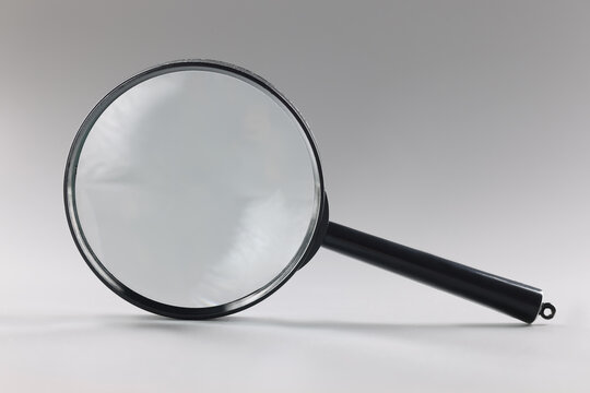 Single magnifying glass with black handle, leaning on grey surface