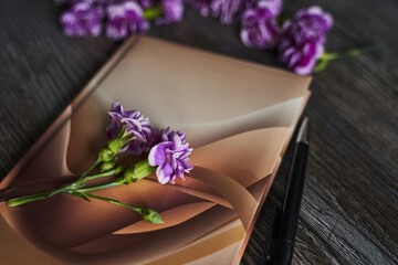 notepad and pen close-up with small purple carnations on a wooden background