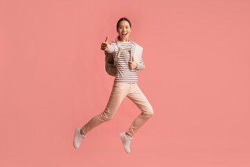 Happy Young Asian Female Student Jumping In Air And Showing Thumb Up