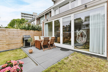 Charming courtyard of the house with a barbecue and a wooden table with upholstered chairs - obrazy, fototapety, plakaty