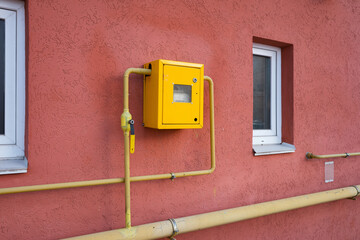 Yellow metal anti vandal box with natural gas meter gauge and pipeline on the wall. Gas distribution for heating apartments in winter.
